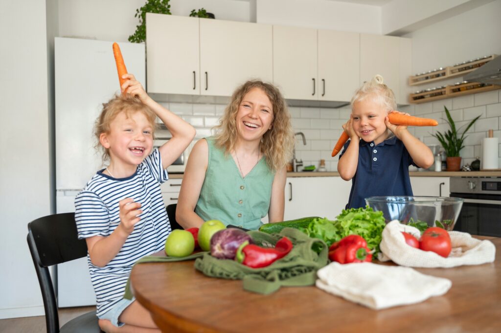 Madre feliz divirtiéndose con sus hijas sosteniendo zanahorias en la cocina de casa